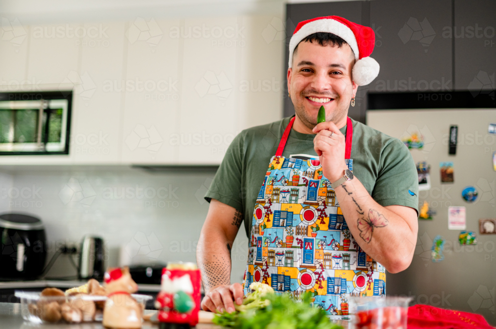A man in a Santa hat smiles while cooking with fresh produce in a vibrant kitchen - Australian Stock Image