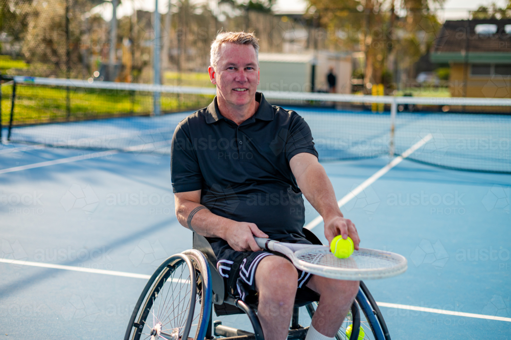 A man in a wheelchair holds a tennis ball on a blue court in Australia - Australian Stock Image