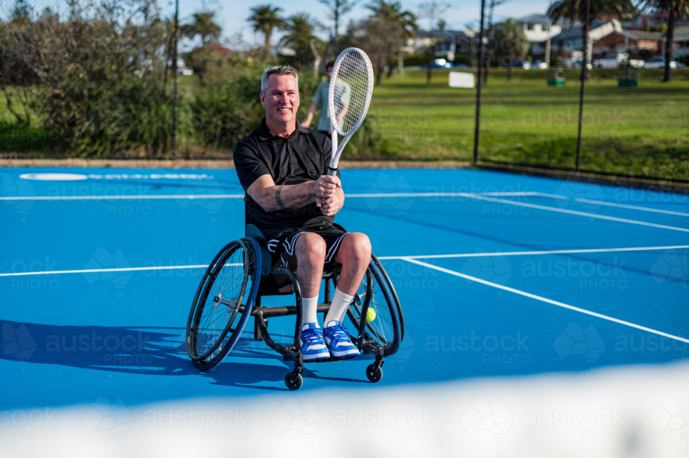 A man in a wheelchair plays tennis on a double formation - Australian Stock Image