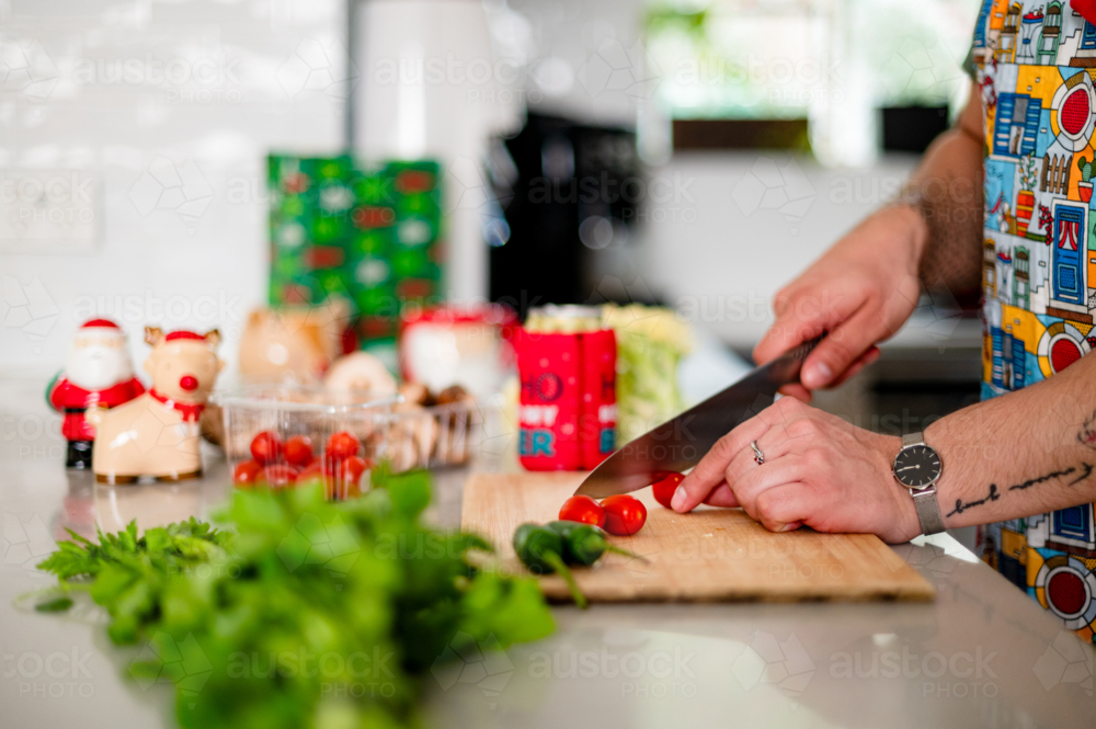 A man in an apron cutting tomatoes in kitchen - Australian Stock Image