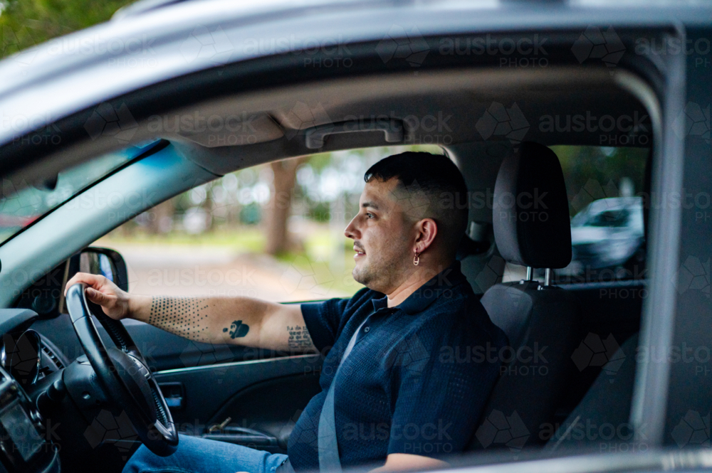 A man in his 30s drives through a peaceful park, enjoying the warm outdoors - Australian Stock Image