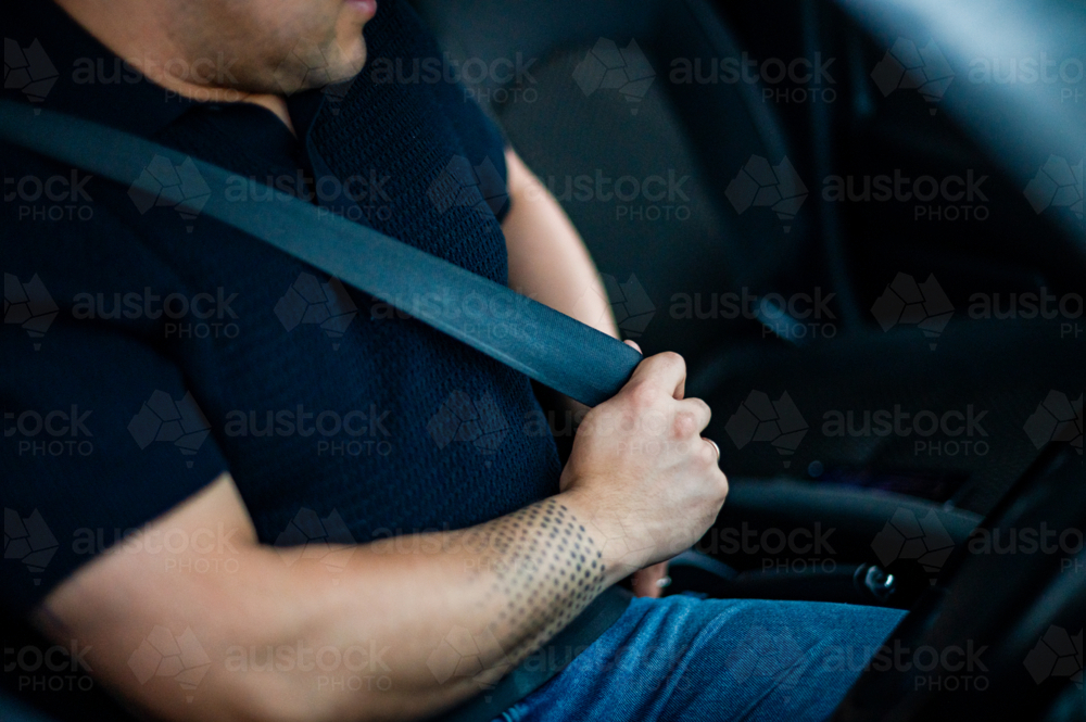 A man in his 30s fastens his seatbelt inside a car parked - Australian Stock Image