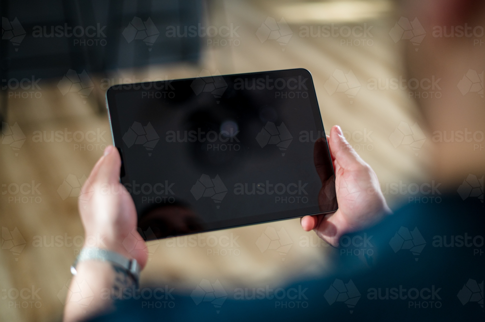 A man in his 30s interacts with a digital tablet in a contemporary living space - Australian Stock Image