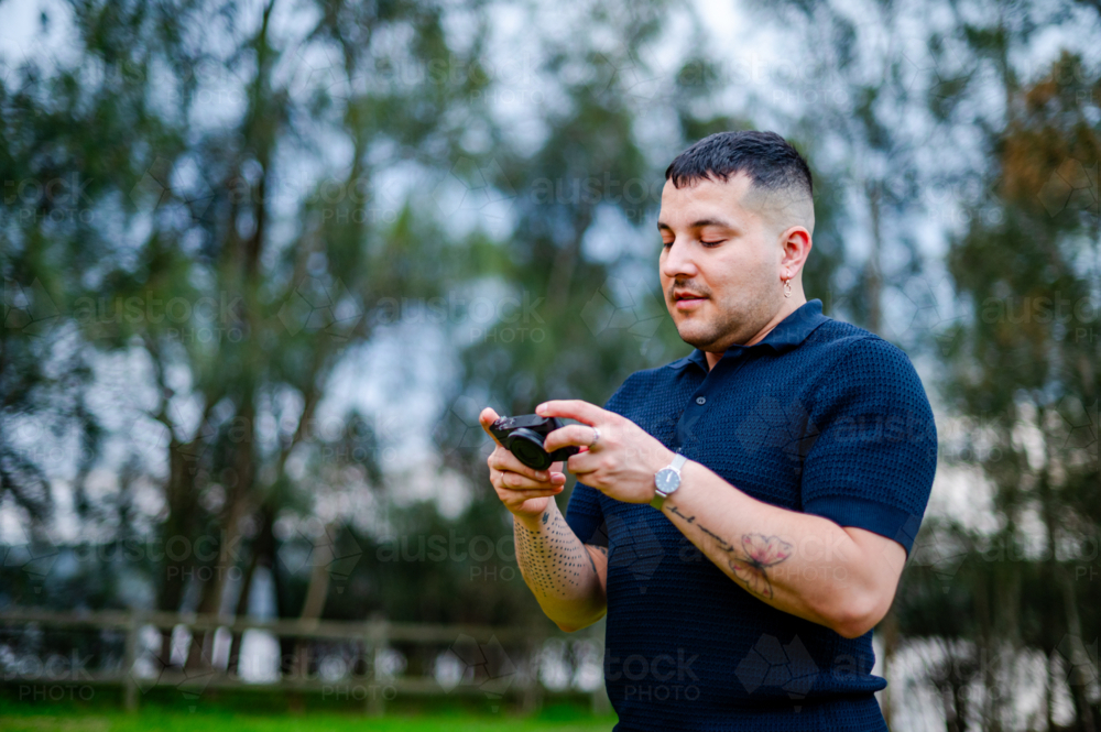 A man in his 30s is capturing outdoor moments with a digital camera in a park - Australian Stock Image