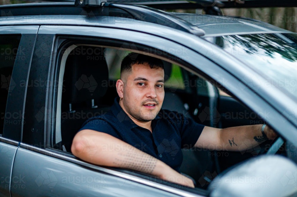 A man in his 30s sits comfortably in his car, smiling while parked in a park. - Australian Stock Image