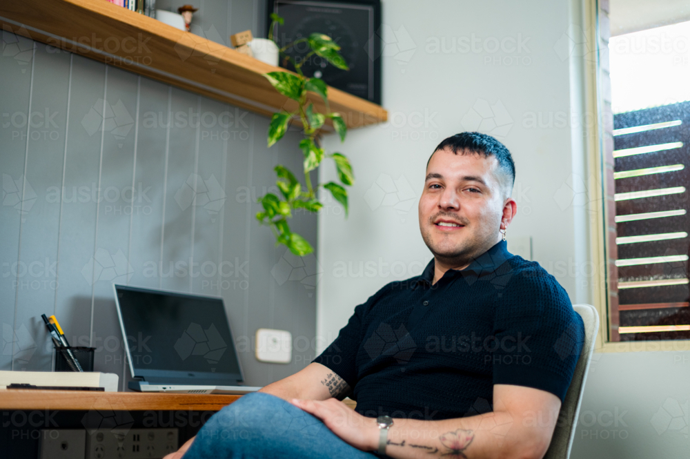 A man in his 30s sitting at a home desk with a computer - Australian Stock Image