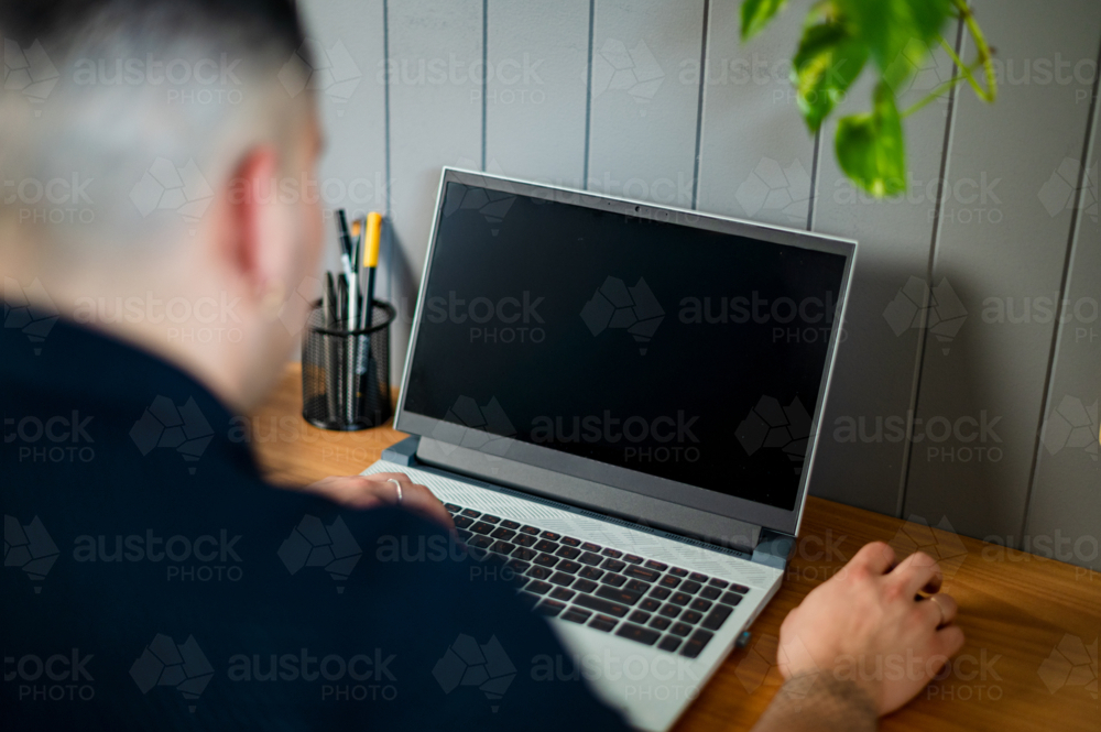 A man in his 30s working on his laptop at home - Australian Stock Image