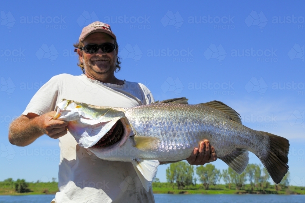 A man in his early forties holds a large (1.14 meter) barramundi before releasing it - Australian Stock Image