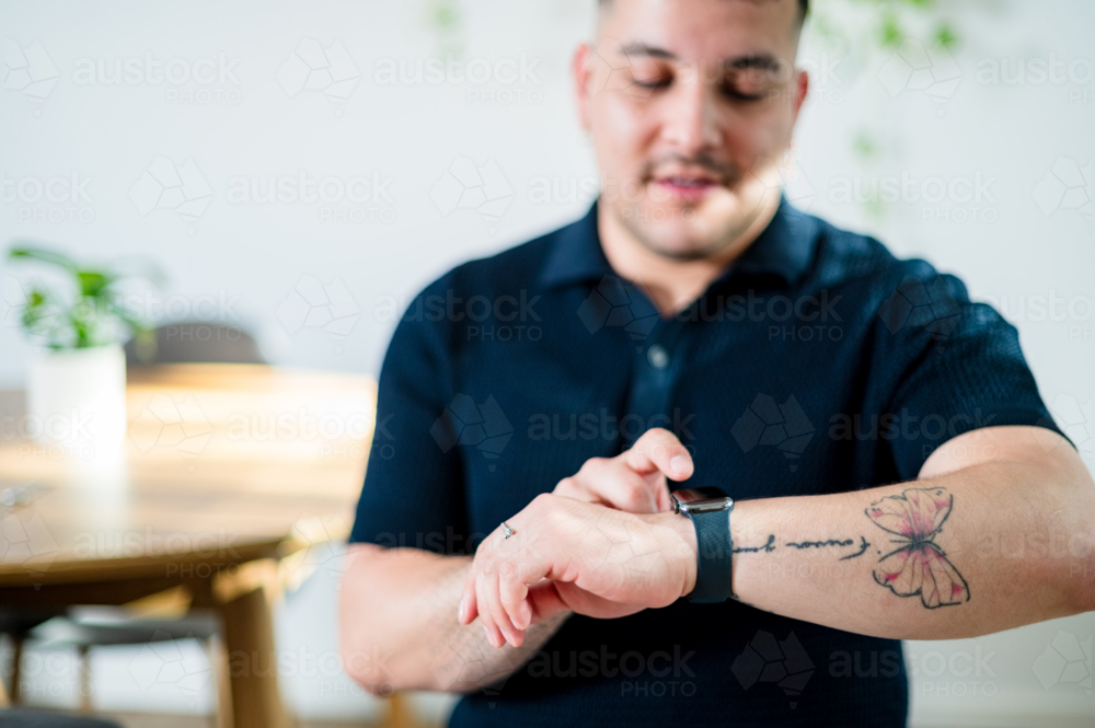 A man in his thirties interacts with his smartwatch in a modern home setting, focused on the device - Australian Stock Image