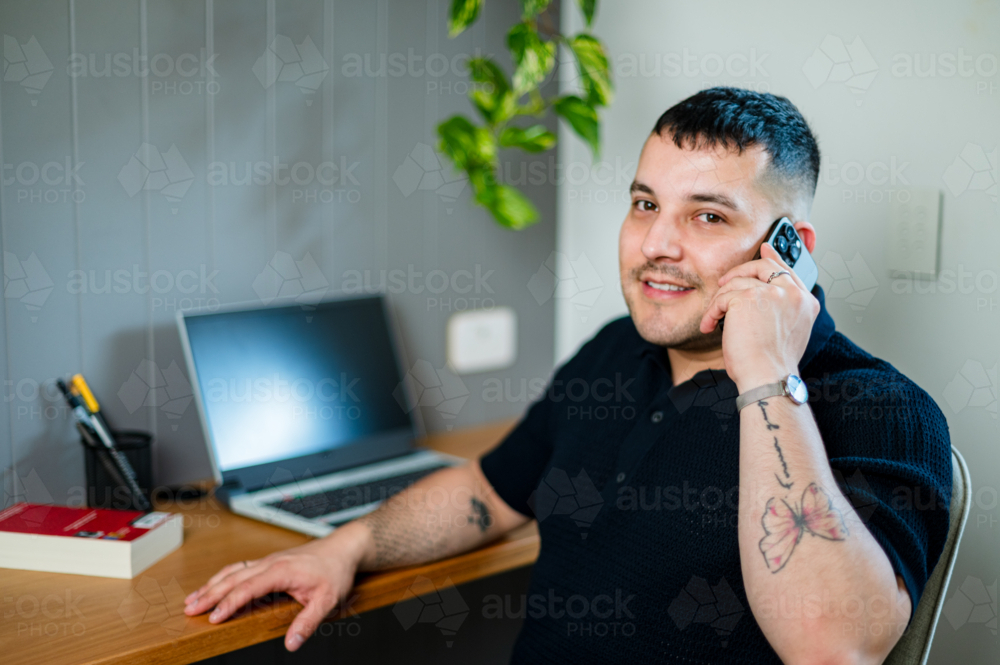 A man in his thirties talking on the phone in a cosy home office - Australian Stock Image