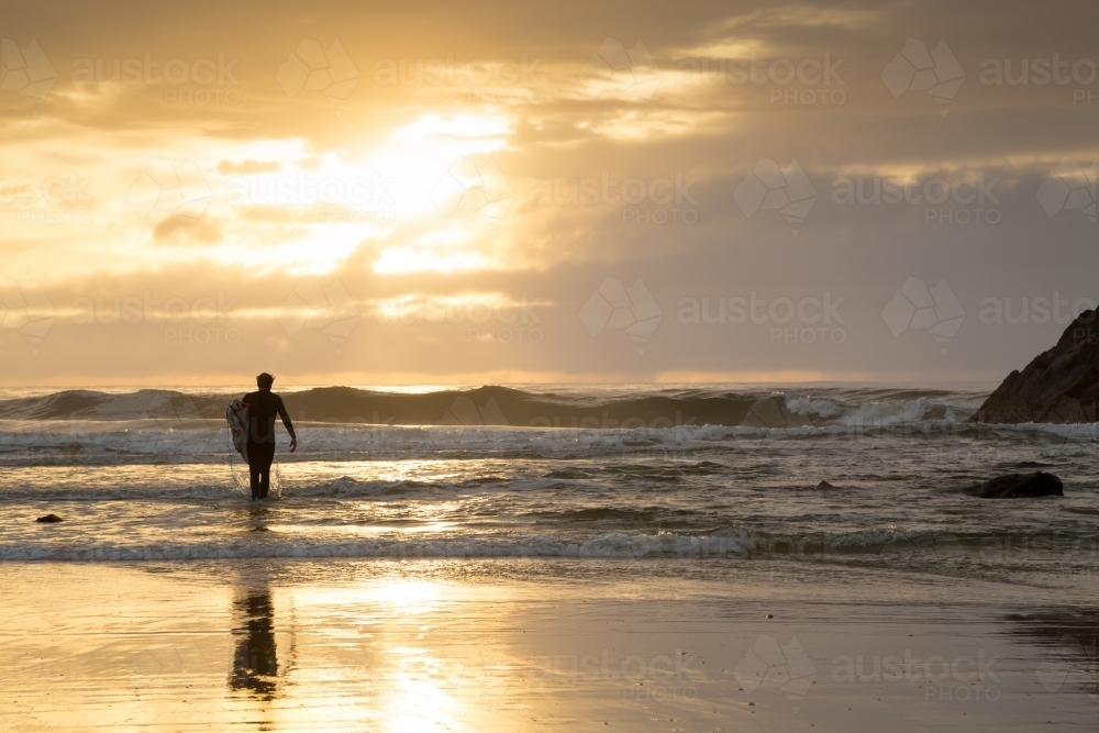 Image of A man in his thirties walking into the surf with surfboard ...