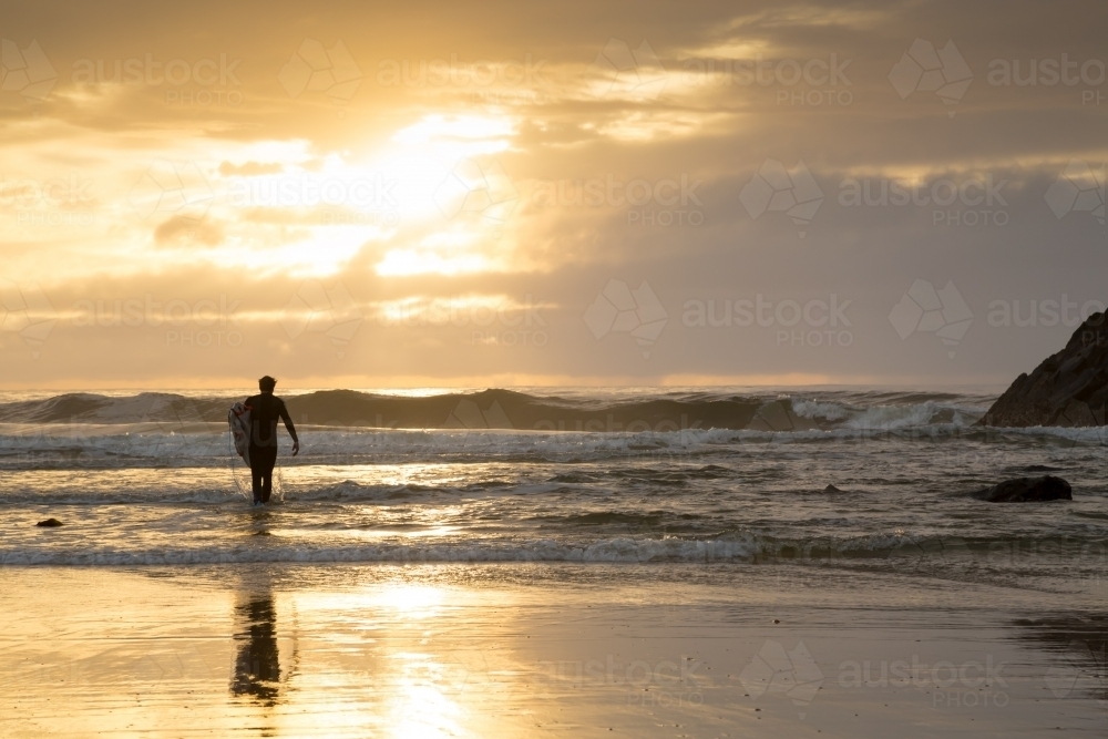 A man in his thirties walking into the surf with surfboard. - Australian Stock Image