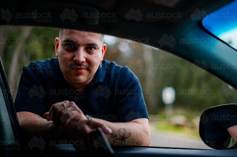 A man leans on a car window form outside vehicle in a park setting - Australian Stock Image