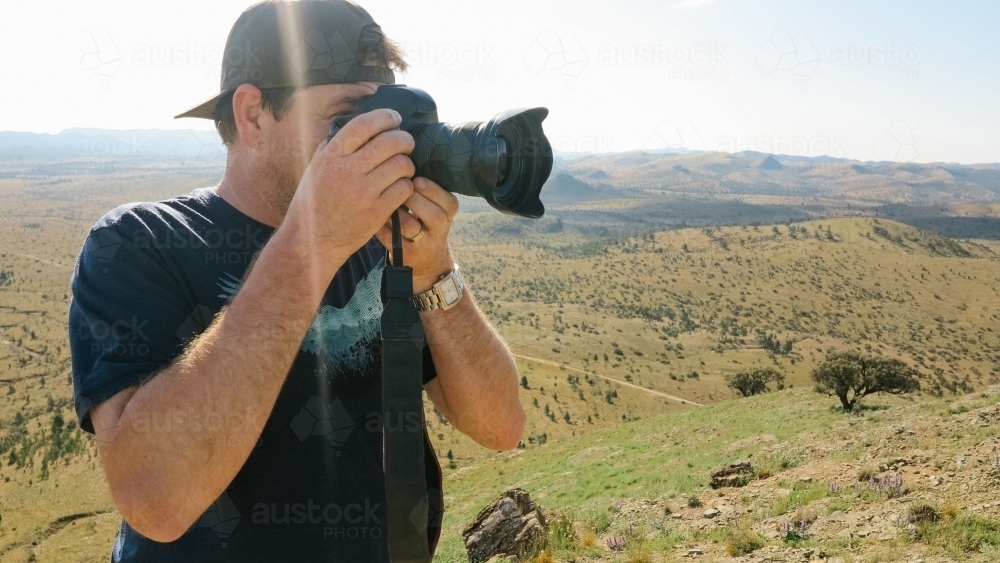 A man looking through the viewfinder of his camera with a vast landscape behind - Australian Stock Image