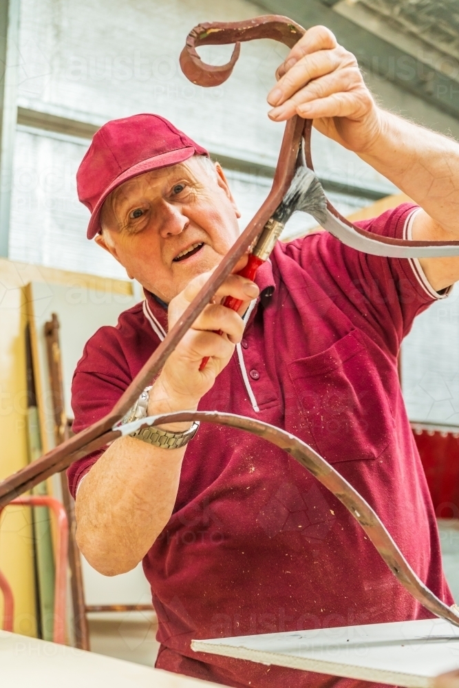 A man painting ironwork at a Men's Shed - Australian Stock Image