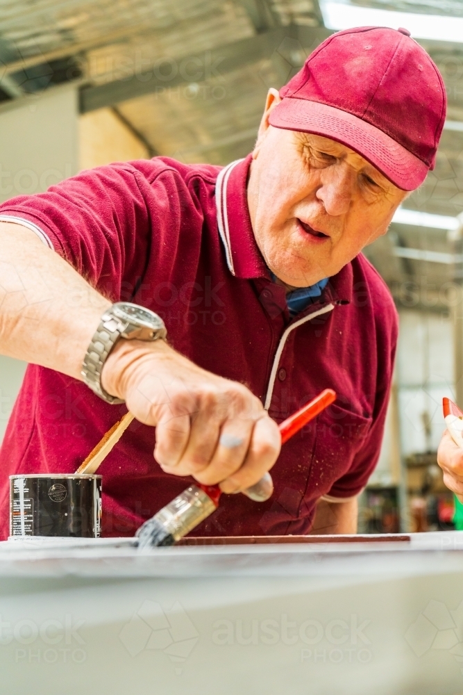 A man painting on a tabletop at a Men's Shed - Australian Stock Image