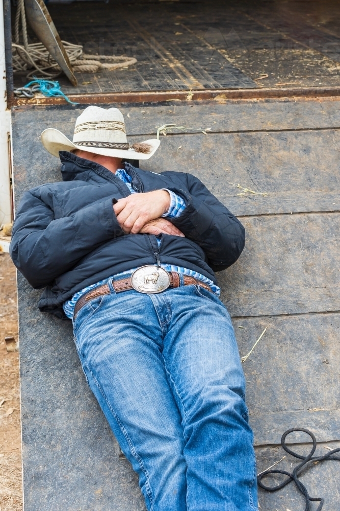 A man sleeping on ramp of a horse float with a hat over his face - Australian Stock Image