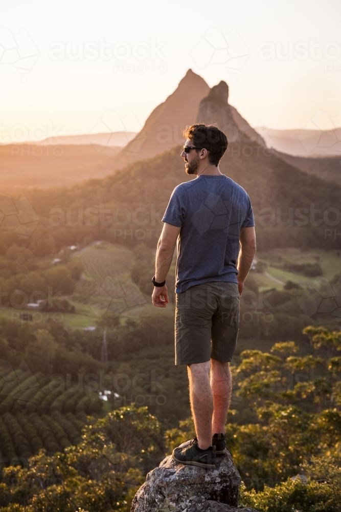 A man stands on a rock overlooking mountains - Australian Stock Image