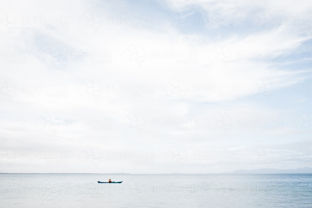 A man using a blue Kayak in the Ocean on a still but cloudy day - Australian Stock Image