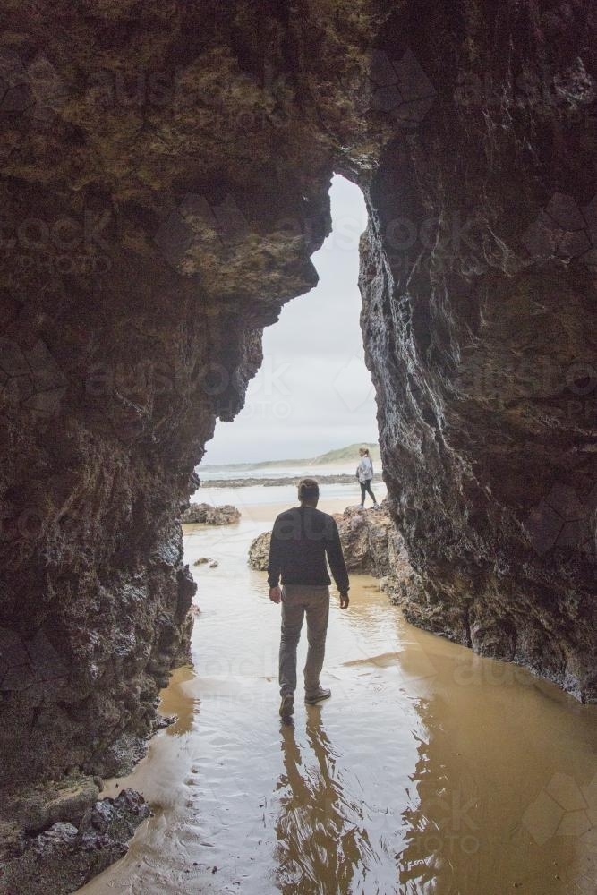 A man walks through a cave on the beach - Australian Stock Image