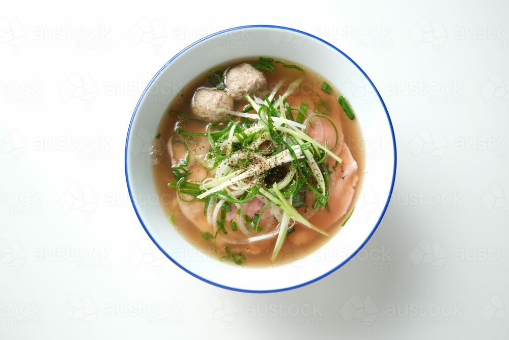 A meatball noodle soup topped with green onions surrounded by spices on the surface. - Australian Stock Image