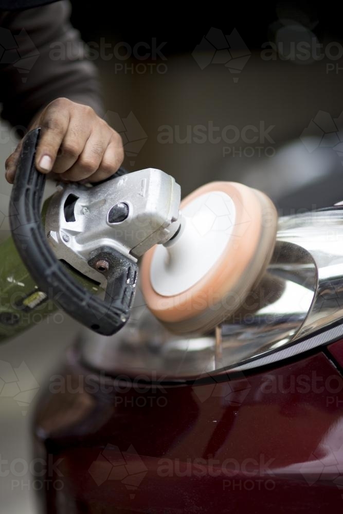 A mechanic buffers the headlight of a vehicle during a routine service. - Australian Stock Image