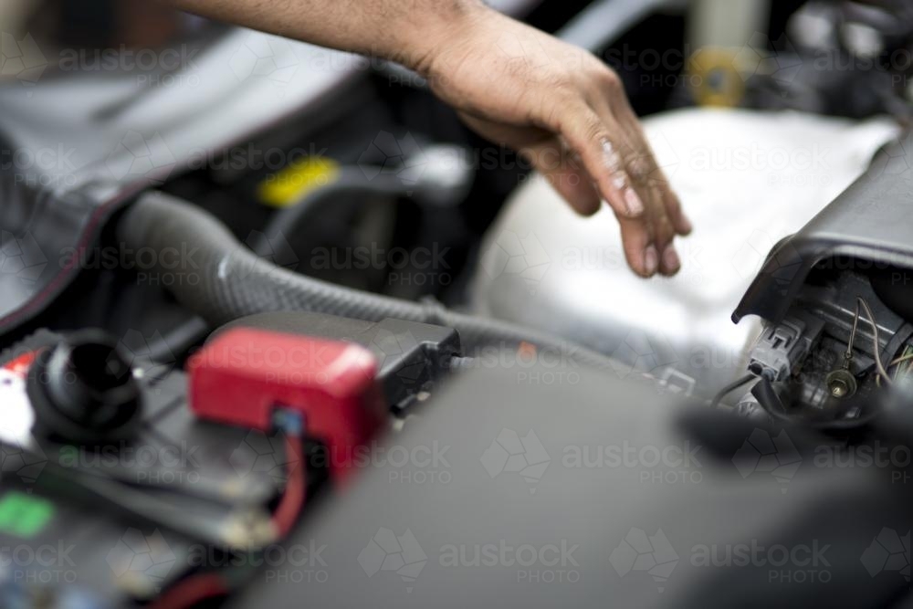 A mechanic reaches into the bonnet of a car during a service. - Australian Stock Image