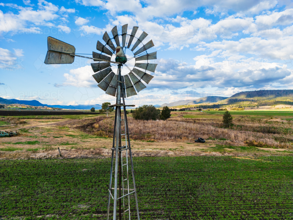 A metal windmill above a field and hilly area in south east Queensland - Australian Stock Image