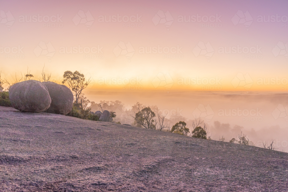 A misty sunrise under pink skies on a granite monolith - Australian Stock Image