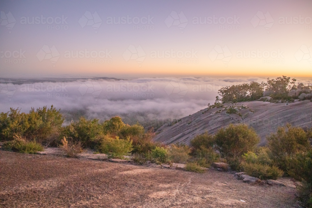 A misty sunrise under pink skies on a granite monolith - Australian Stock Image