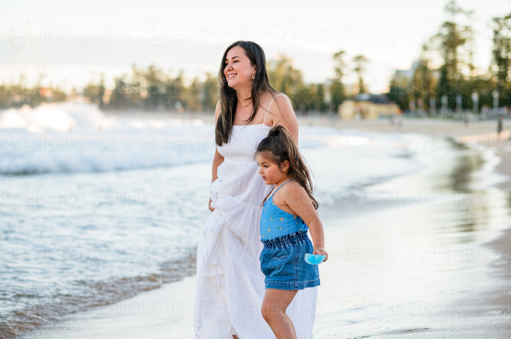 A mother and daughter enjoy time together on the beach as waves crash nearby - Australian Stock Image
