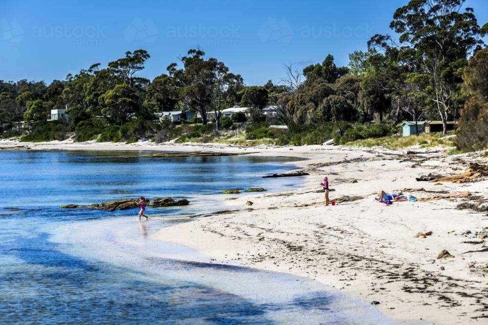 A mother and kids play on the beach in a sheltered cove - Australian Stock Image
