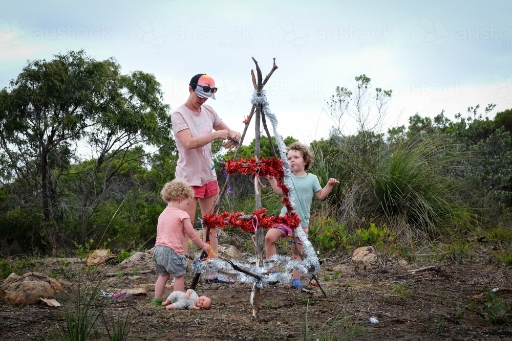 A mother and two toddlers celebrating Christmas decorating a rustic Christmas tree - Australian Stock Image
