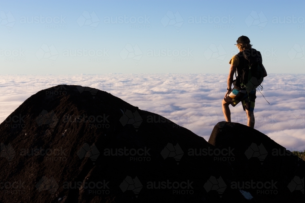 A mountaineer looks over a view above the cloud tops from the summit of a mountain - Australian Stock Image