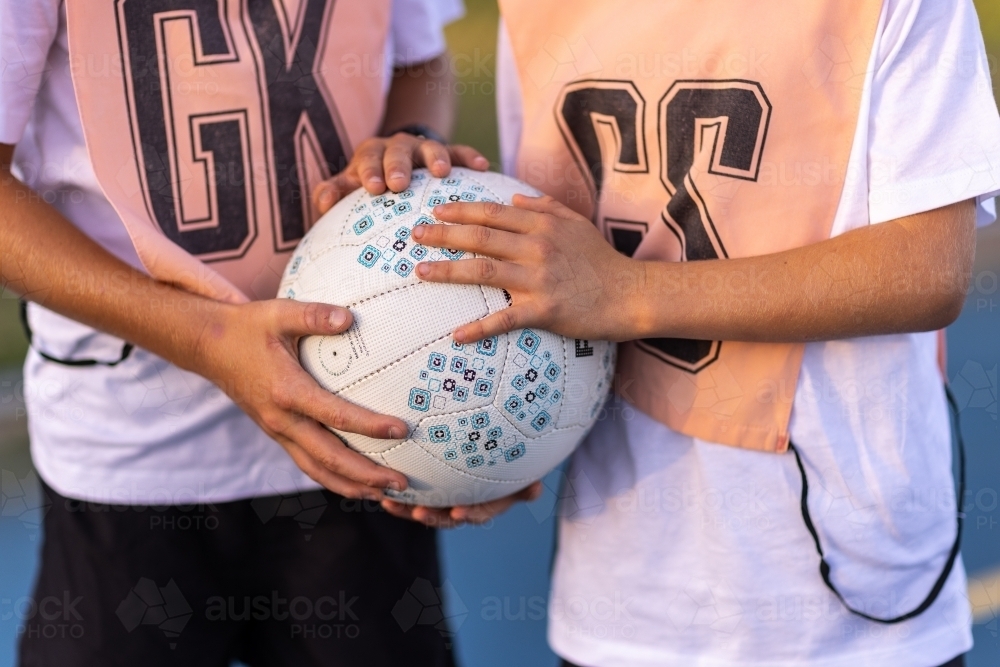 a netball being held by two kids wearing netball bibs - Australian Stock Image