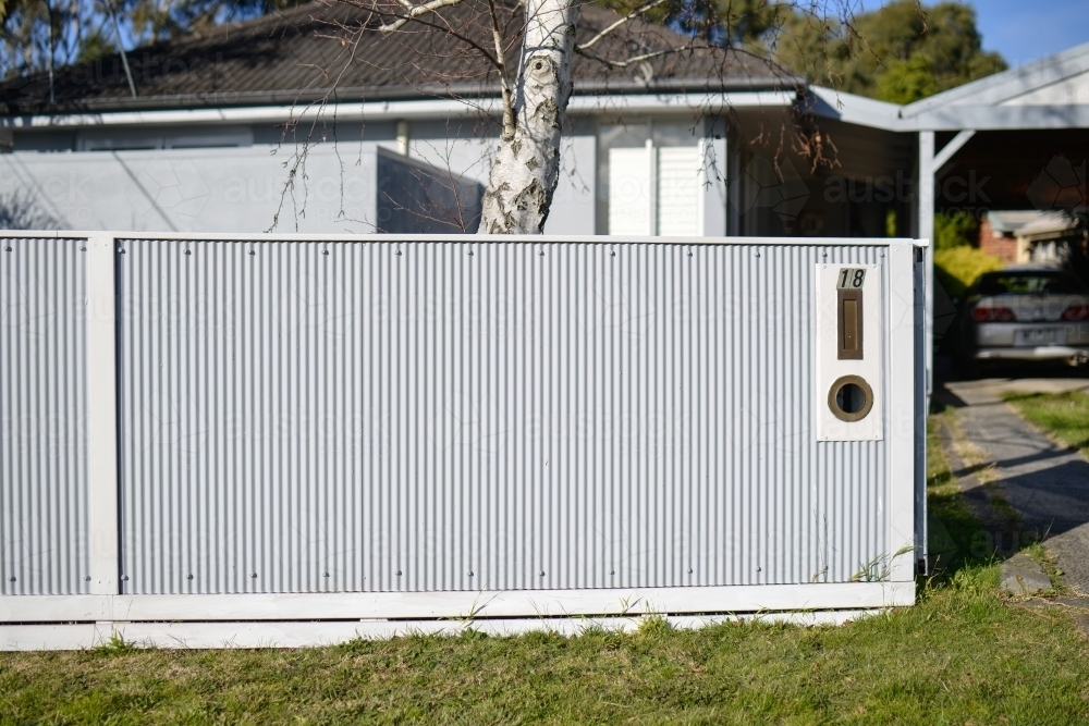 A new white corrugated fence in front of a single storey house - Australian Stock Image