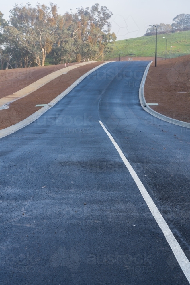 Image of A newly laid bitumen road leading over a rise through a new ...