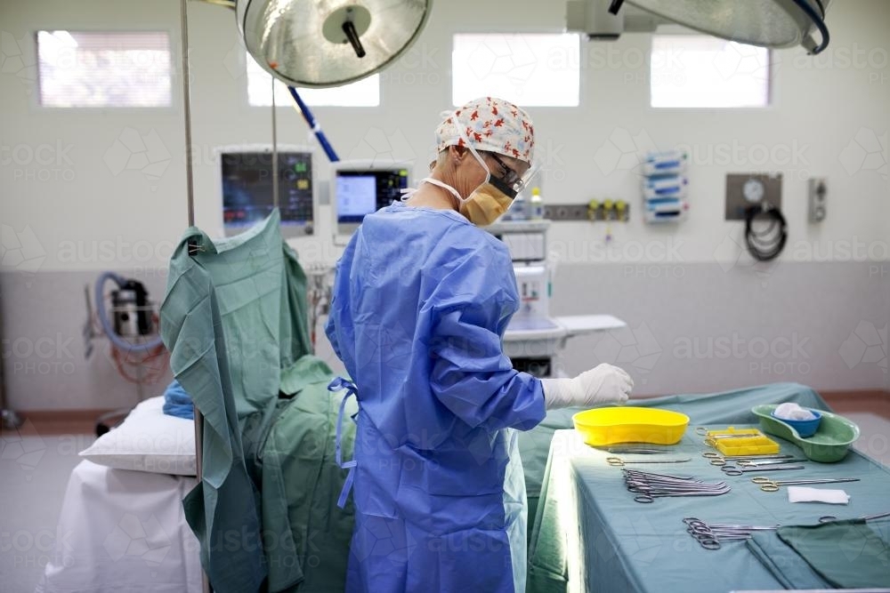 A nurse in a hospital operating theatre with table of surgical equipment - Australian Stock Image
