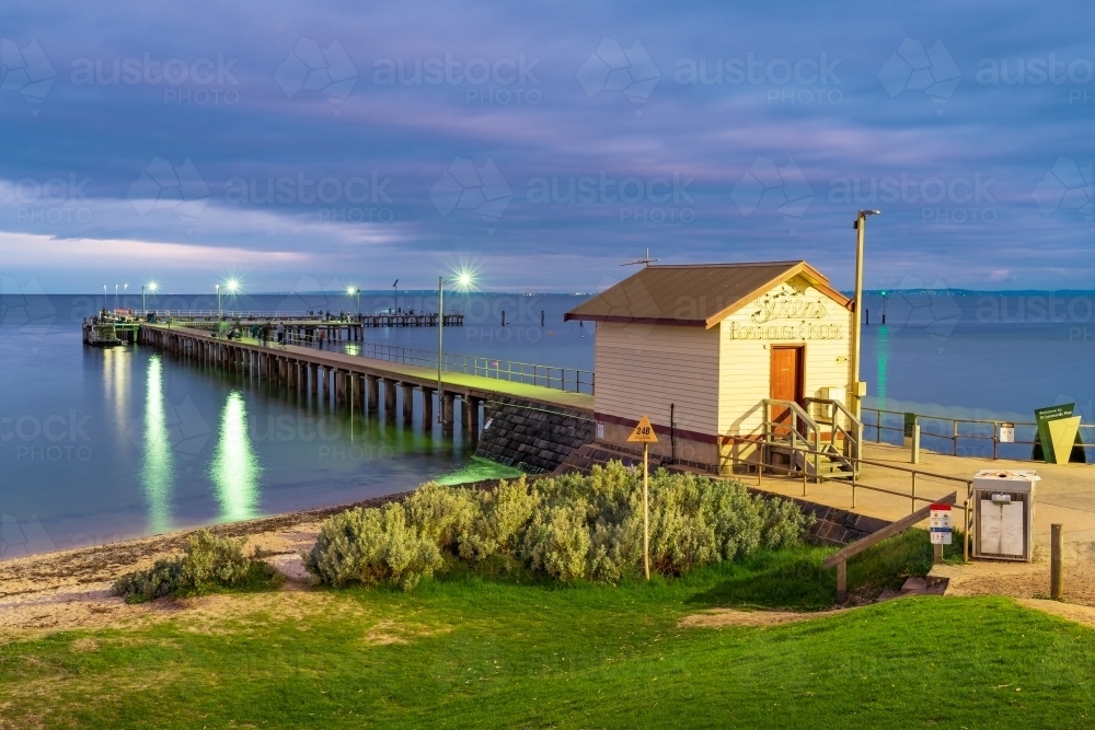 A old wooden kiosk at the entrance to a coastal jetty under an overcast sky at twilight - Australian Stock Image
