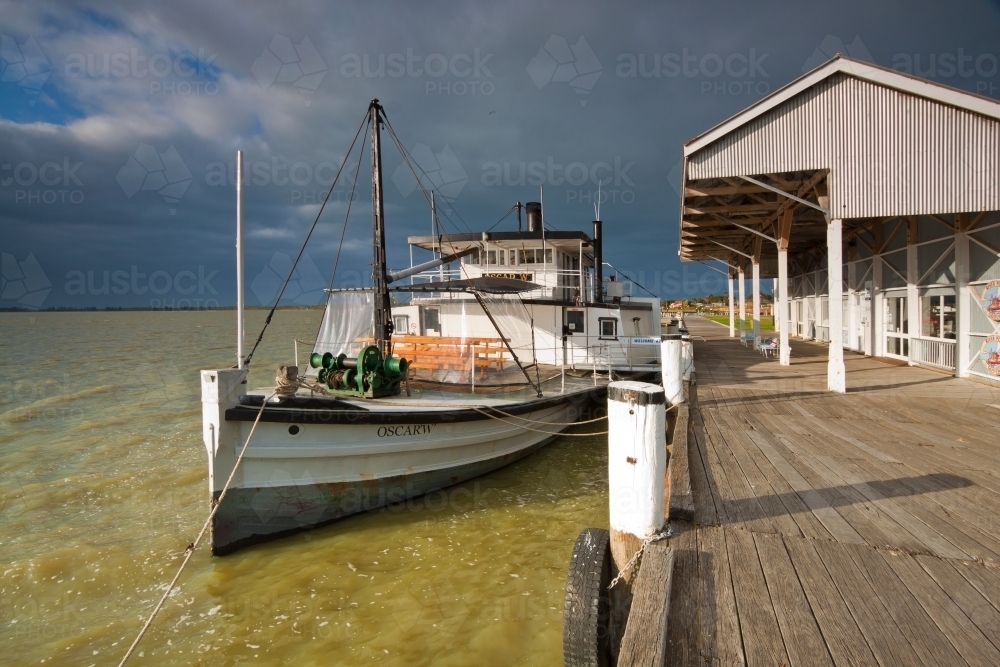 A paddle steamer tied to a wharf under a dark morning sky - Australian Stock Image