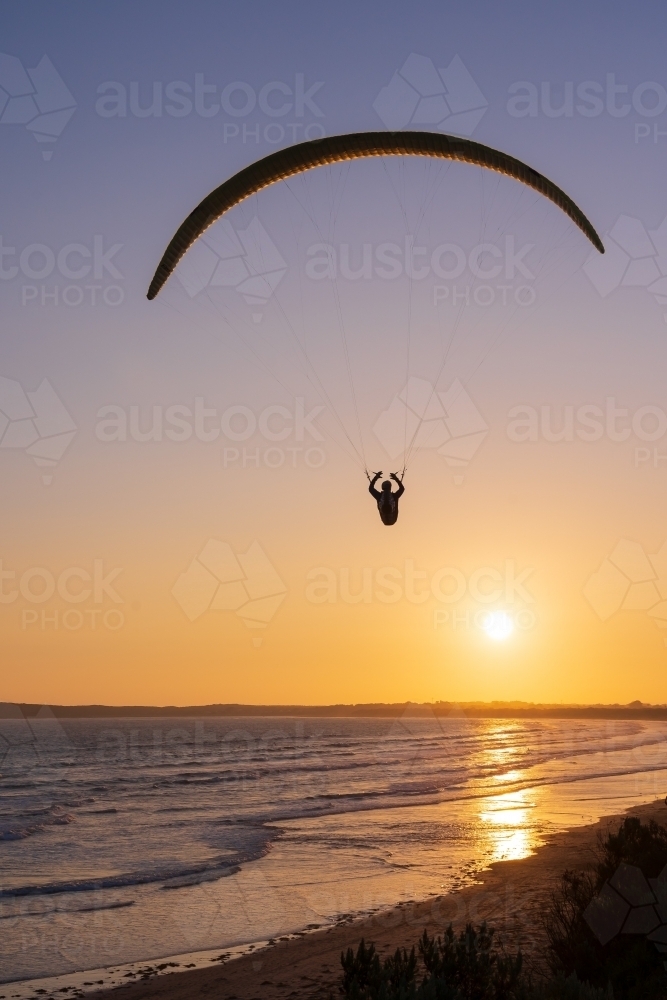 A paraglider in the sky at sunset over the beach - Australian Stock Image