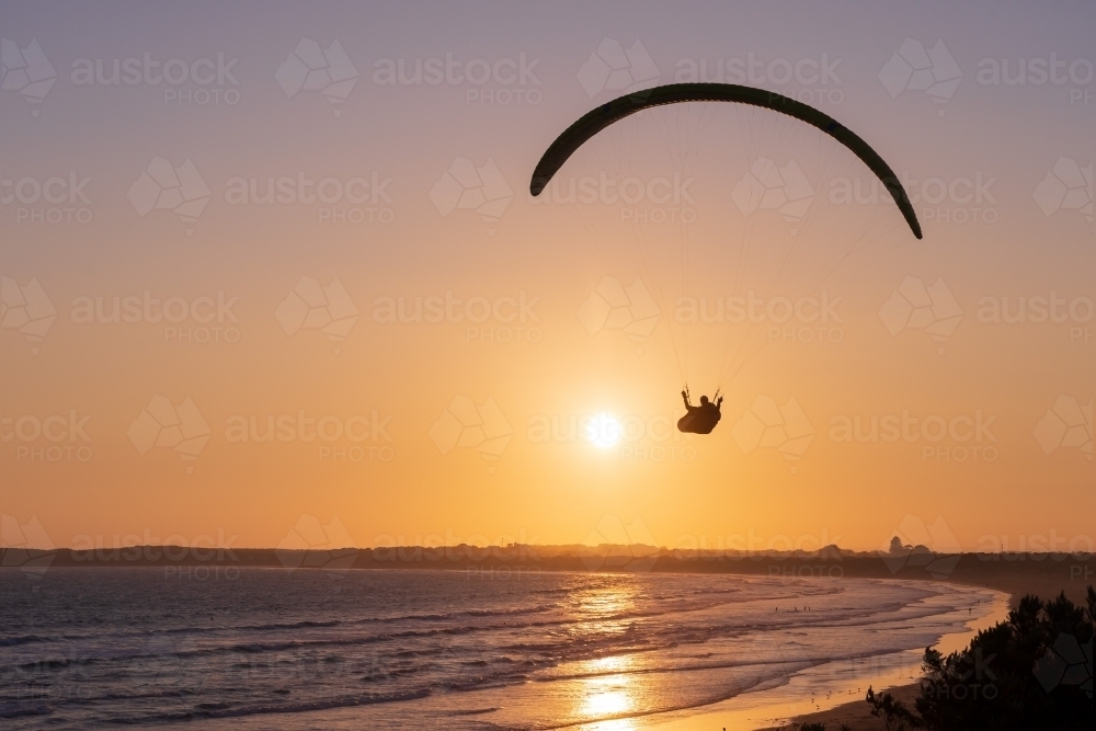 A paraglider in the sky at sunset over the beach - Australian Stock Image