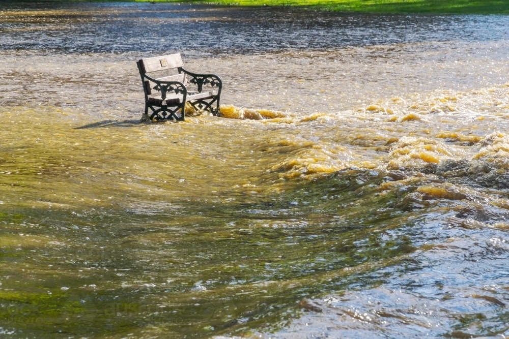 A park bench sits in rushing flood waters - Australian Stock Image