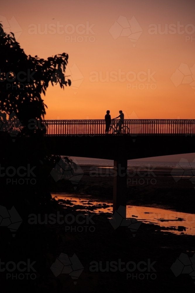 A pedestrian and cyclist on a bridge at sunset - Australian Stock Image