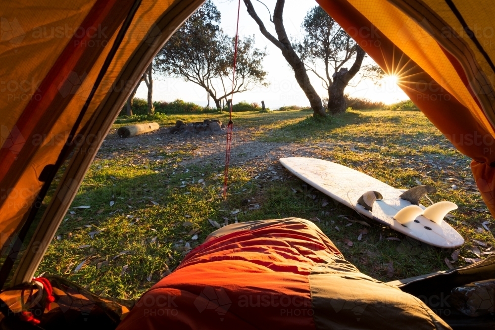 A person in a sleeping bag with a beautiful point of view from a tent with bright morning sun light. - Australian Stock Image