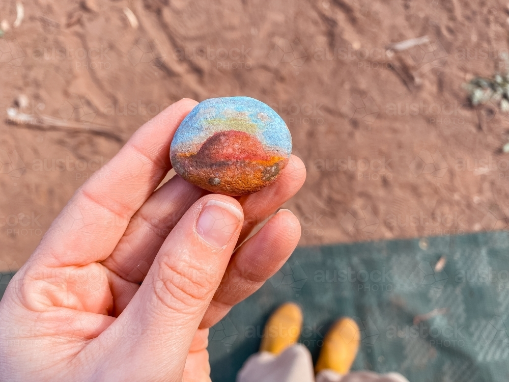 A person’s hand holding a small, round, colourful painted stone. - Australian Stock Image