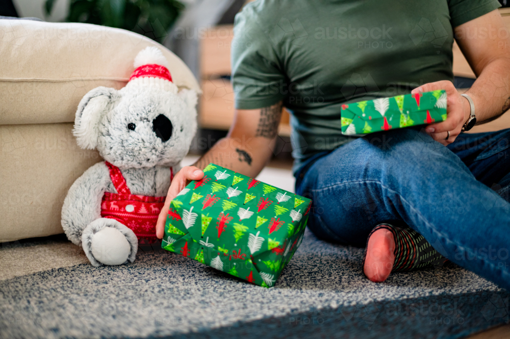 A person sits on the floor with colourful gifts beside a festive koala decoration - Australian Stock Image