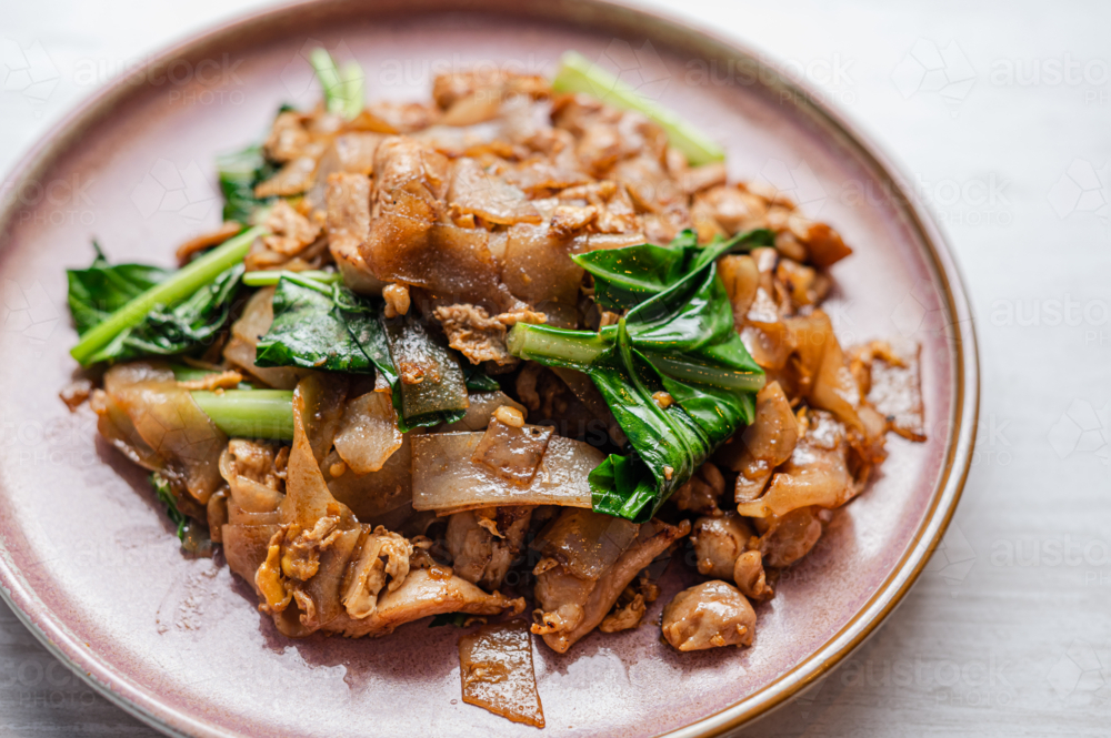 A plate displays stir-fried rice noodles mixed with tender beef, fresh greens, and savoury sauce - Australian Stock Image