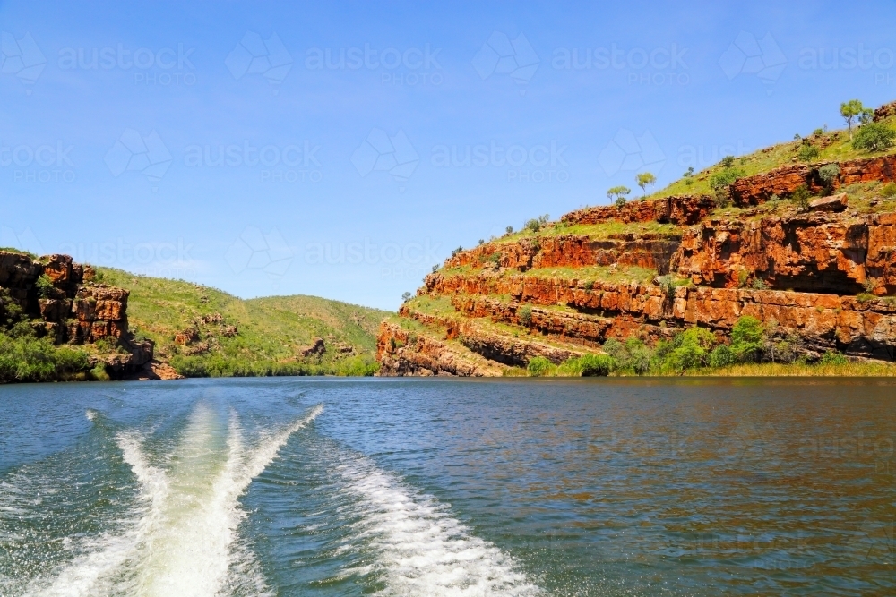 A powerboat wake past red bluffs on Lake Kununurra - Australian Stock Image