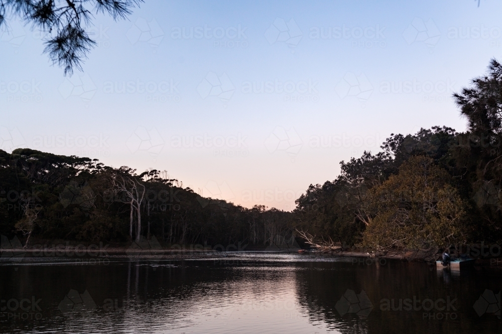 A quiet lake at dusk surround by bush and tree with small boats docked on the right. - Australian Stock Image